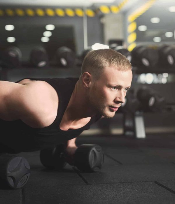 Young man fitness workout, push ups or plank Young man workout in fitness club. Closeup portrait of caucasian guy making plank or push ups exercise on dumbbells, training indoors, copy space